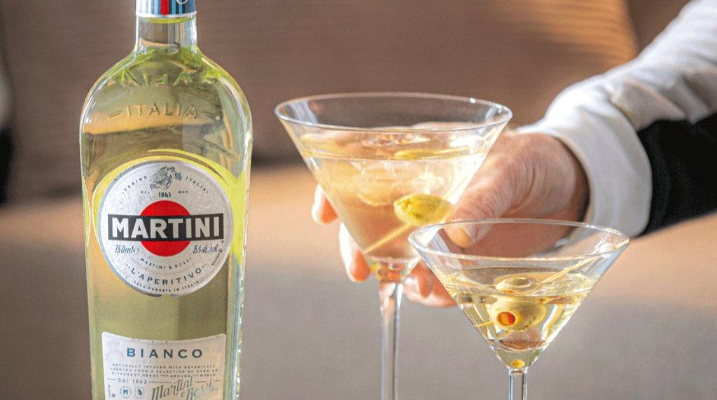 Martini Bianco bottle with two glasses of cocktail held by a person.